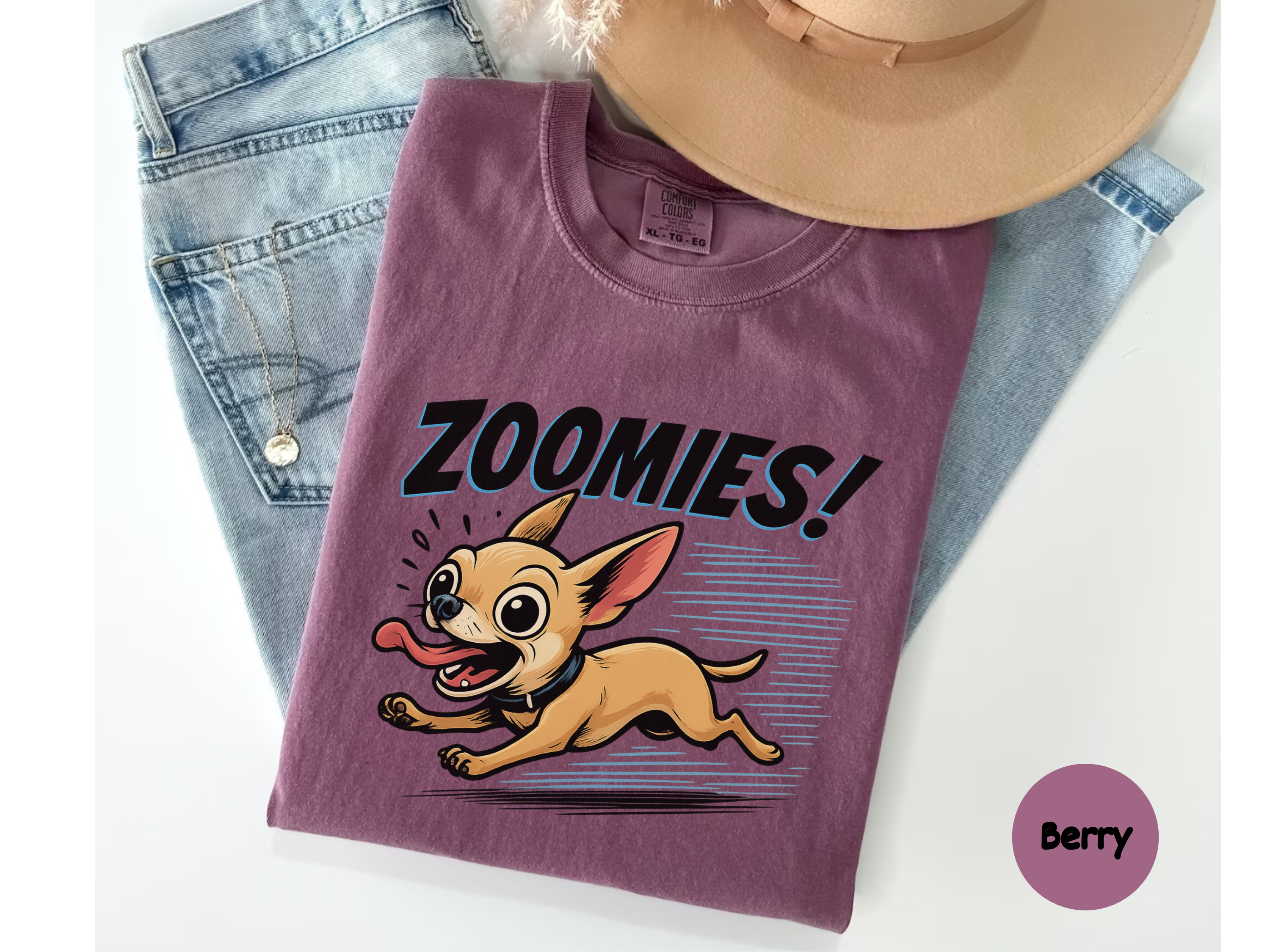 Folded purple t-shirt with cartoon chihuahua dog and 'Zoomies!' text on a white background