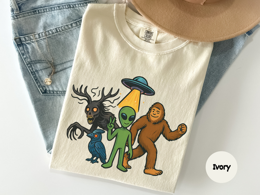 Funny cryptid graphic tee showing an alien under a UFO beam beside Bigfoot and a wendigo with internet conspiracy theme