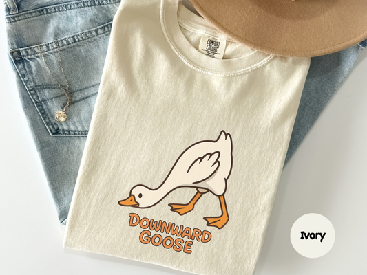 Close up of a black t shirt showing a white goose bending into a yoga pose labeled Downward Goose designed for fitness enthusiasts yoga instructors and fans of playful workout apparel