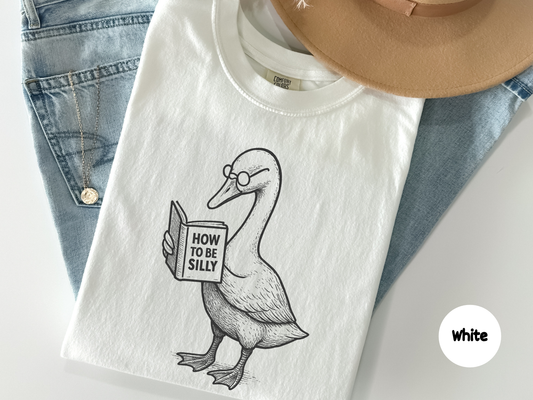 Cute animal graphic tee displaying a goose studying a book called How to Be Silly ideal for bookworms librarians introverts and anyone who loves clever funny reading themed designs