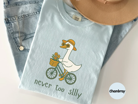 Wholesome animal graphic tee displaying a cartoon goose biking with flowers and the caption Never Too Silly ideal for people who love gentle humor soft fashion and cheerful everyday wear
