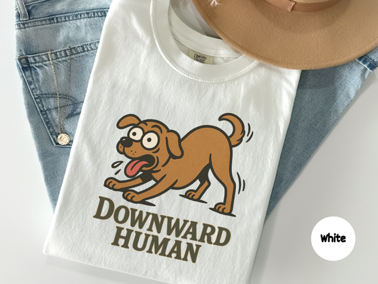 Funny t shirt featuring a cartoon dog stretching in a yoga pose with the words Downward Human on a black background perfect for dog lovers yoga fans and anyone who enjoys animal fitness humor