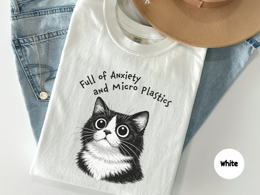 Black and white tuxedo cat illustration with wide anxious eyes printed on a t shirt featuring a cute nervous expression that represents anxiety humor for overthinkers